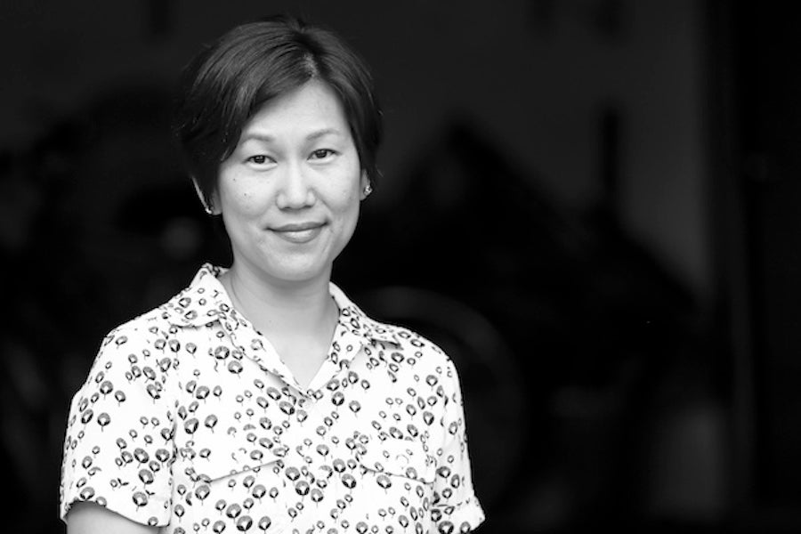 Jennifer Kwon Dobbs, an Asian woman with light skin and short dark hair, smiling, wearing a white print shirt, b/w film, black background