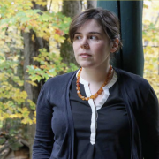 Emily Maloney, white woman with dark brown hair pulled up and back, standing against a leafy backdrop