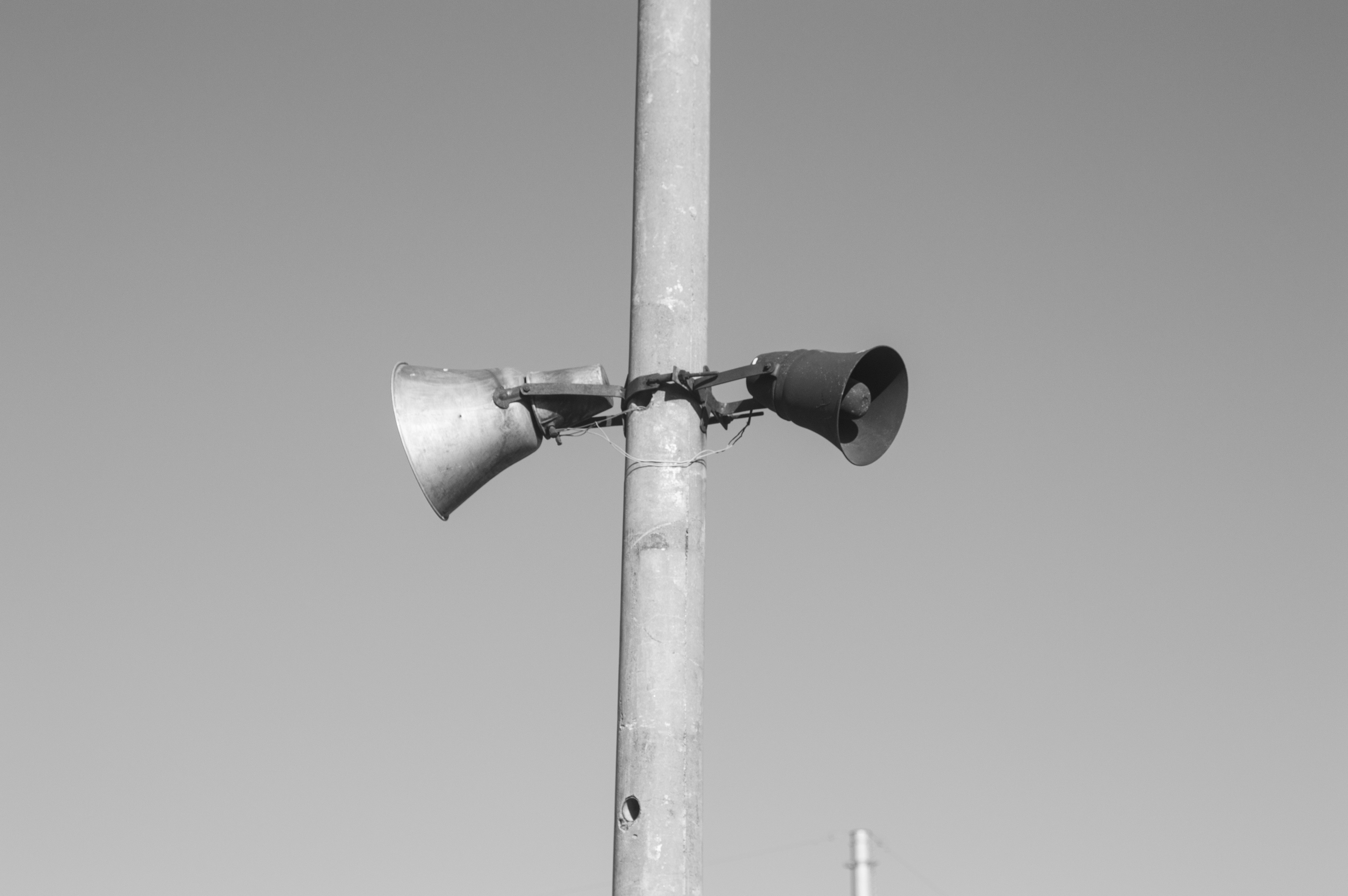 Black and white photo of two battered loudspeakers high up on a pole