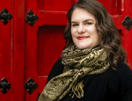 Shannon Reed, white woman with long brown hair, stands in front of red Heinz Chapel doors