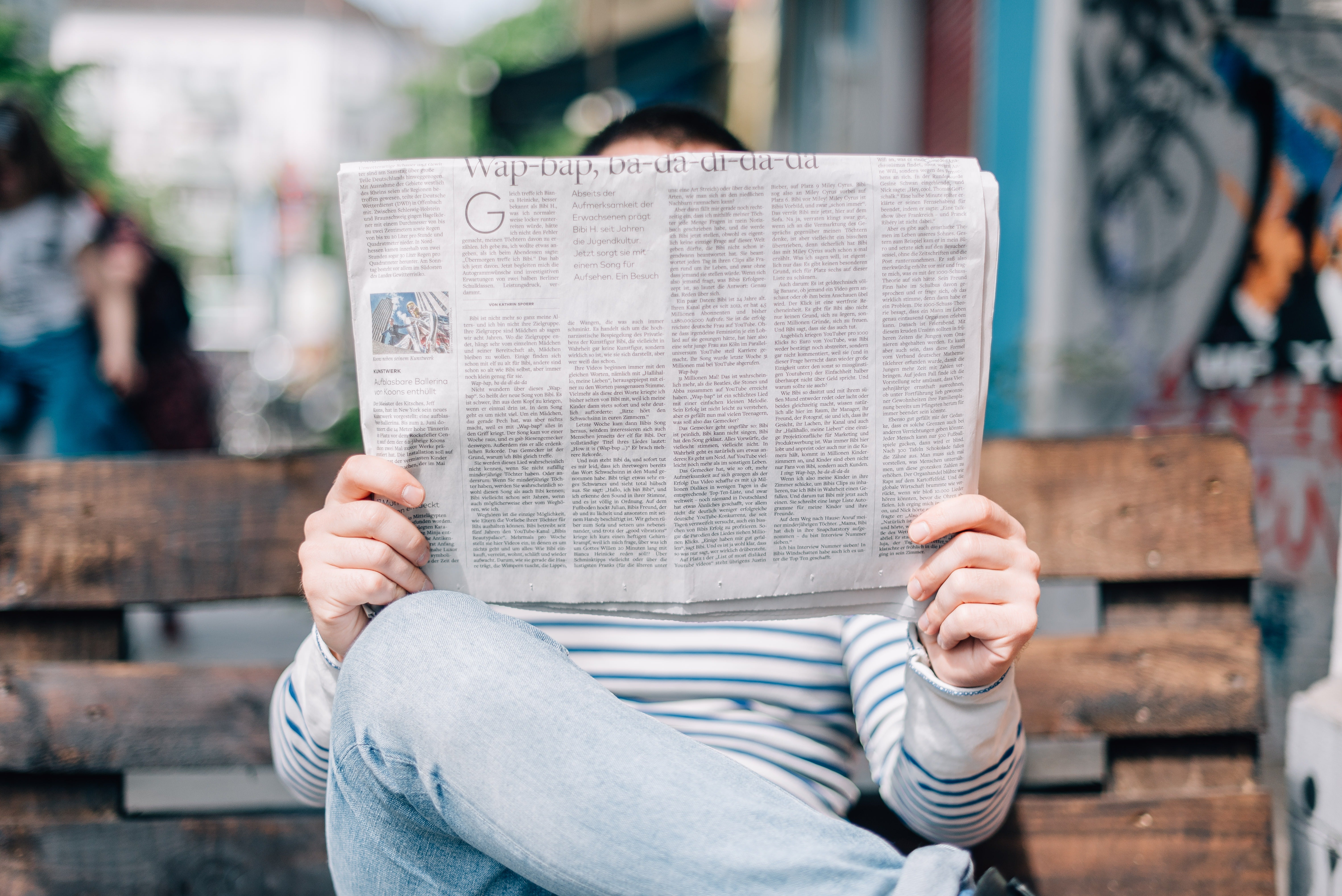 Photo of a person sitting on a bench, newspaper blocking their face.