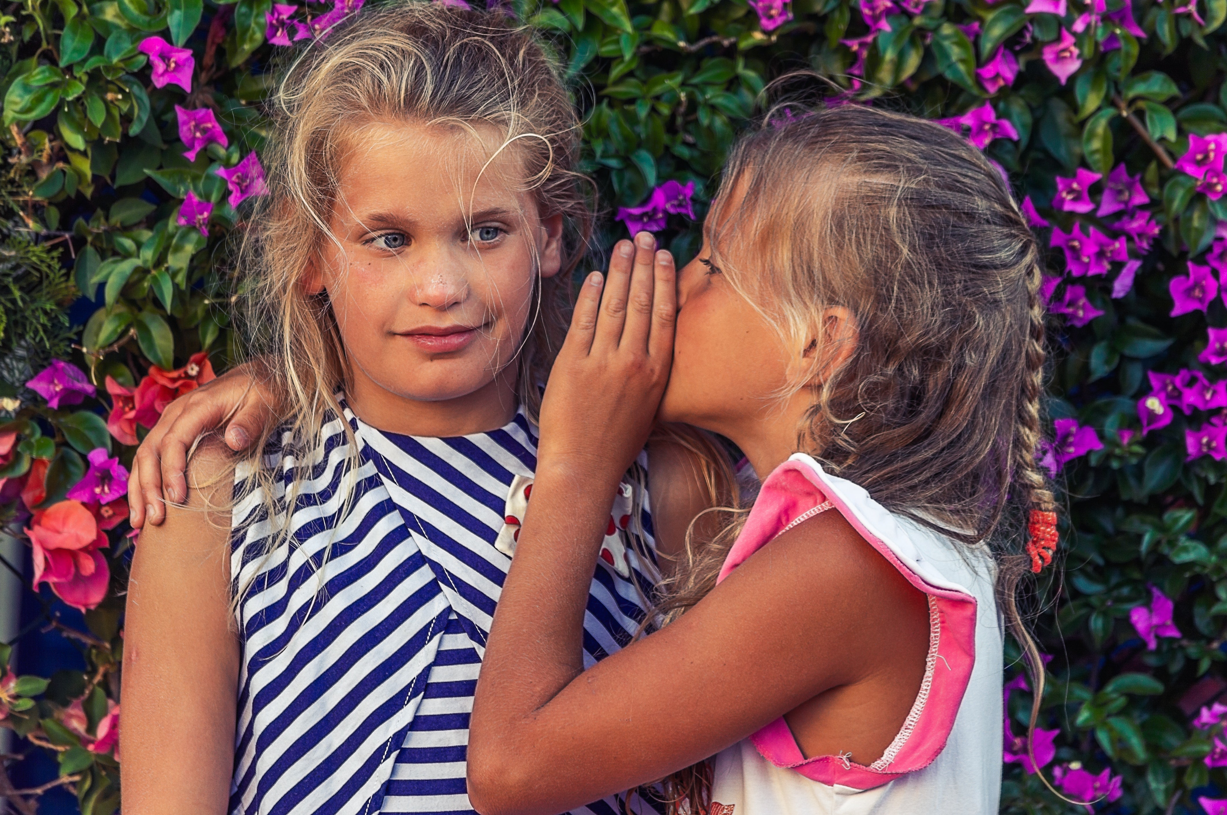 Two young girls, one whispering in the other's ear